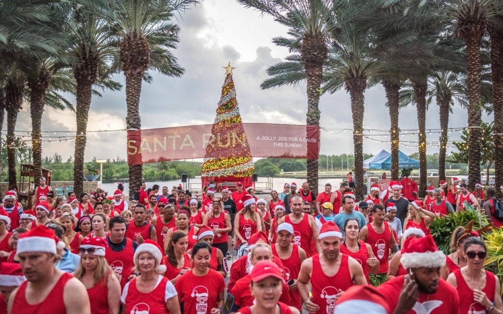 Group of people running in red holiday-themed shirts in front of a Christmas Tree in Camana Bay