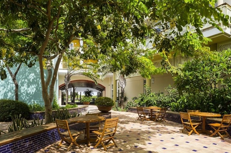 shaded-courtyard -with-cassisa-tress-and-yellow-stools