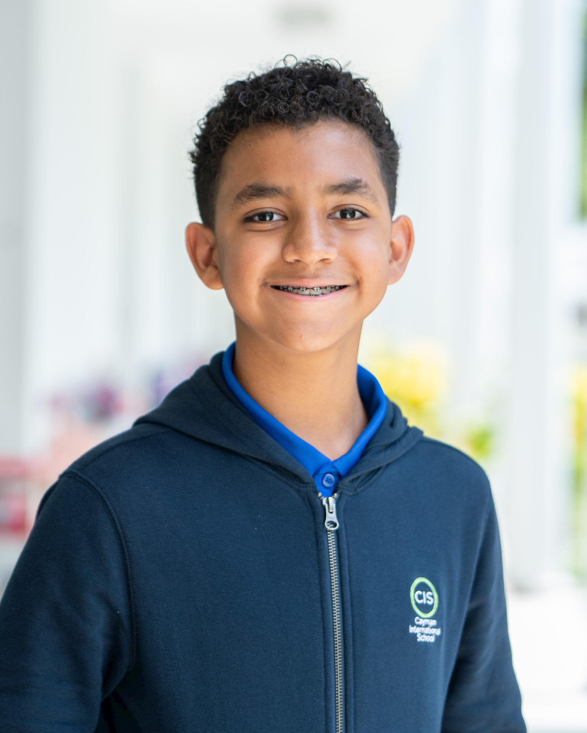 Pre-teen boy with brown skin and black hair, wearing a navy sweater, smiles at the camera.
