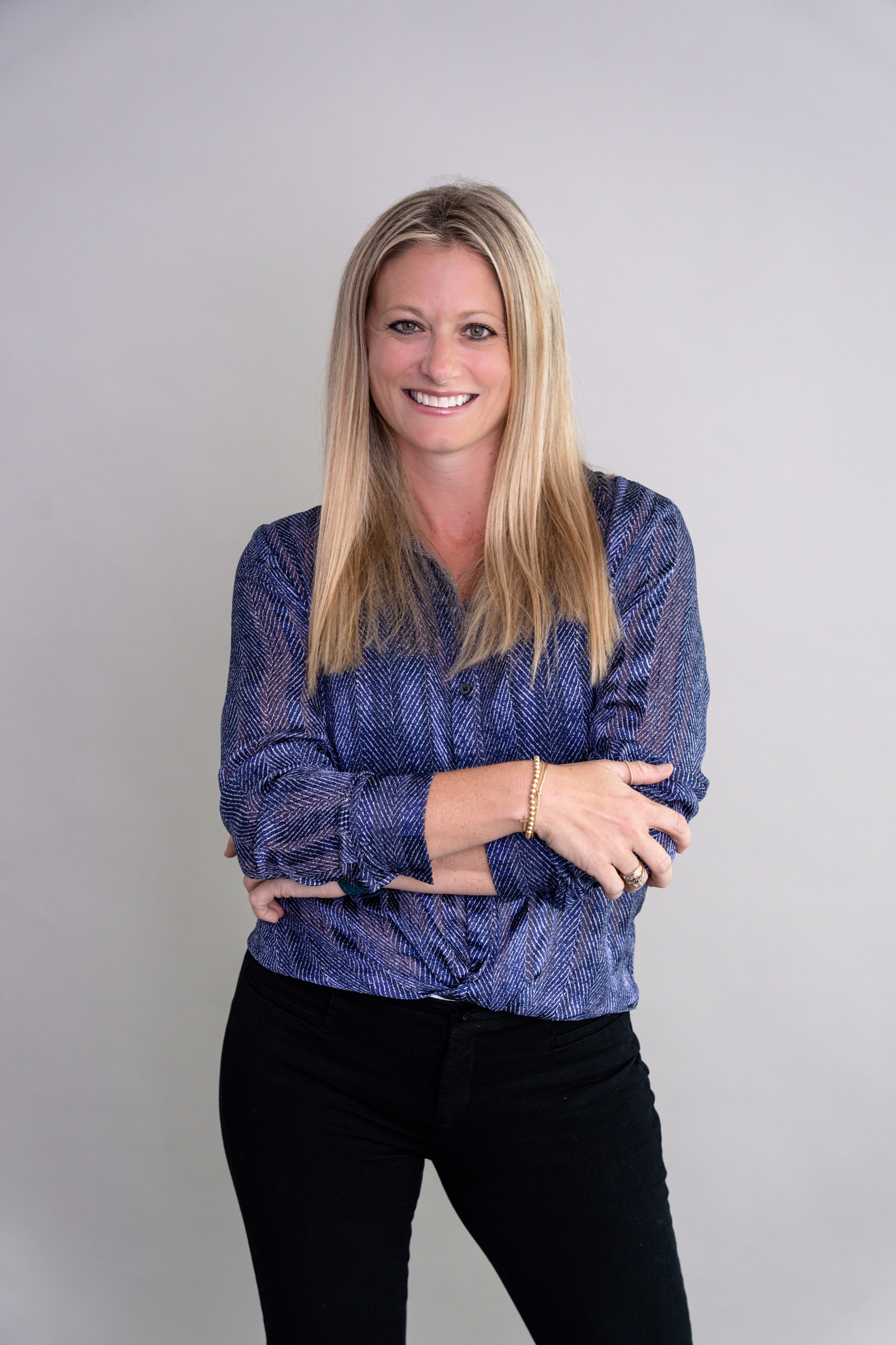 blonde lady stands arms crossed smiles at camera