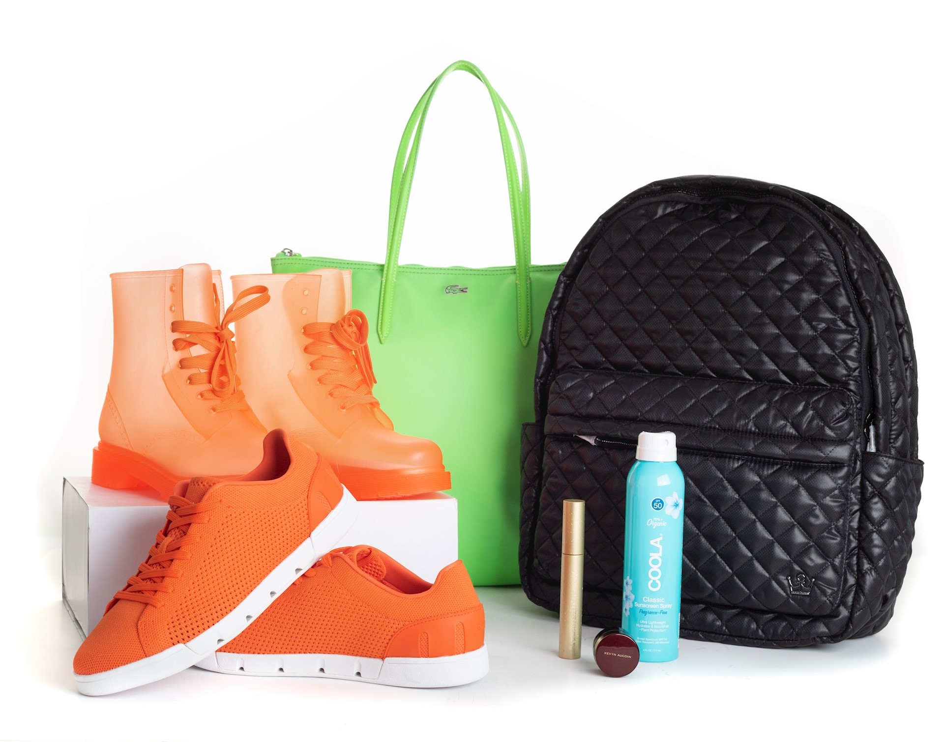 Orange sneakers, Organge Rainboots, Green Purse, Black Backpack and three waterproof makeup products in front of a white background