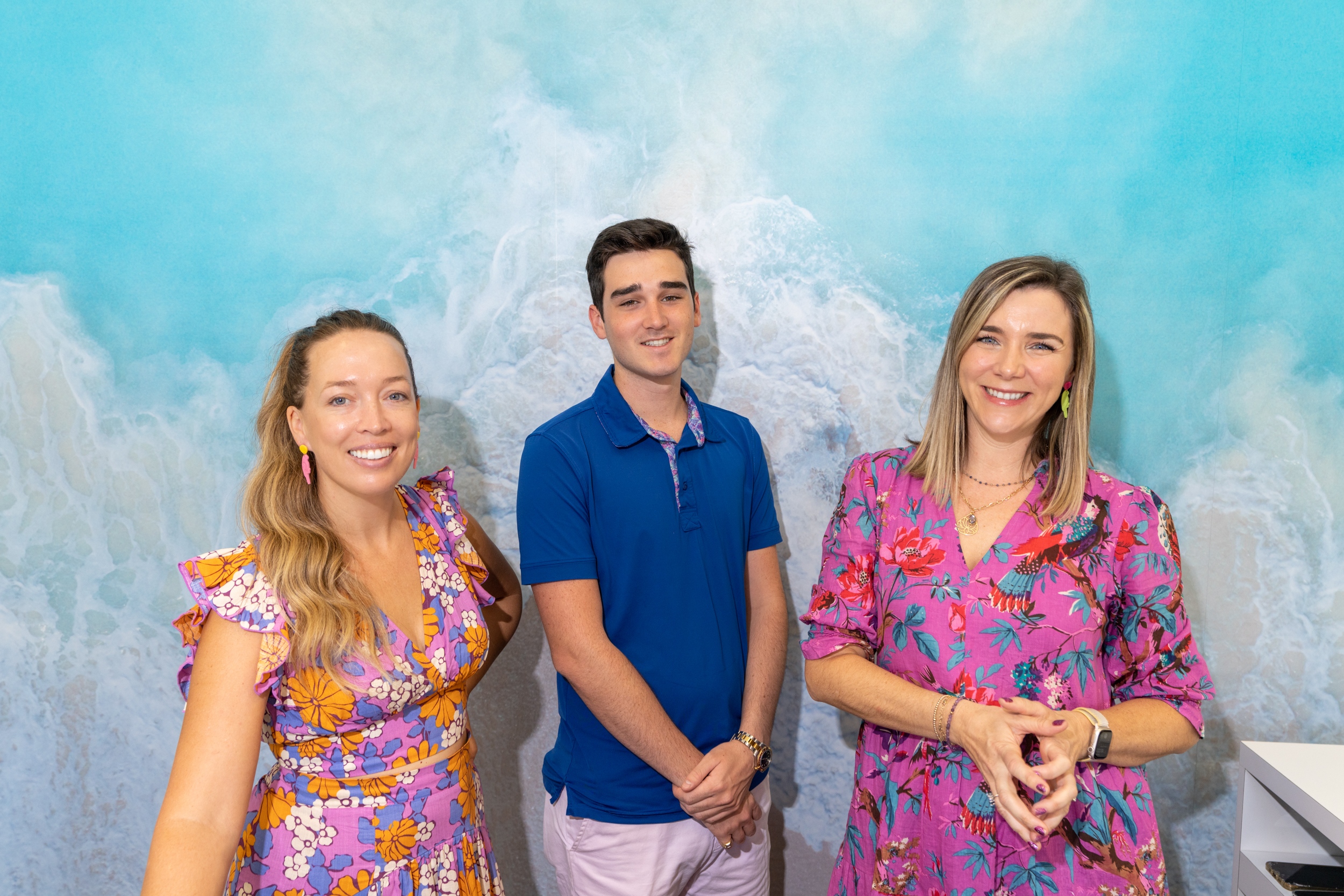 Two women and man pose in front of blue wall.