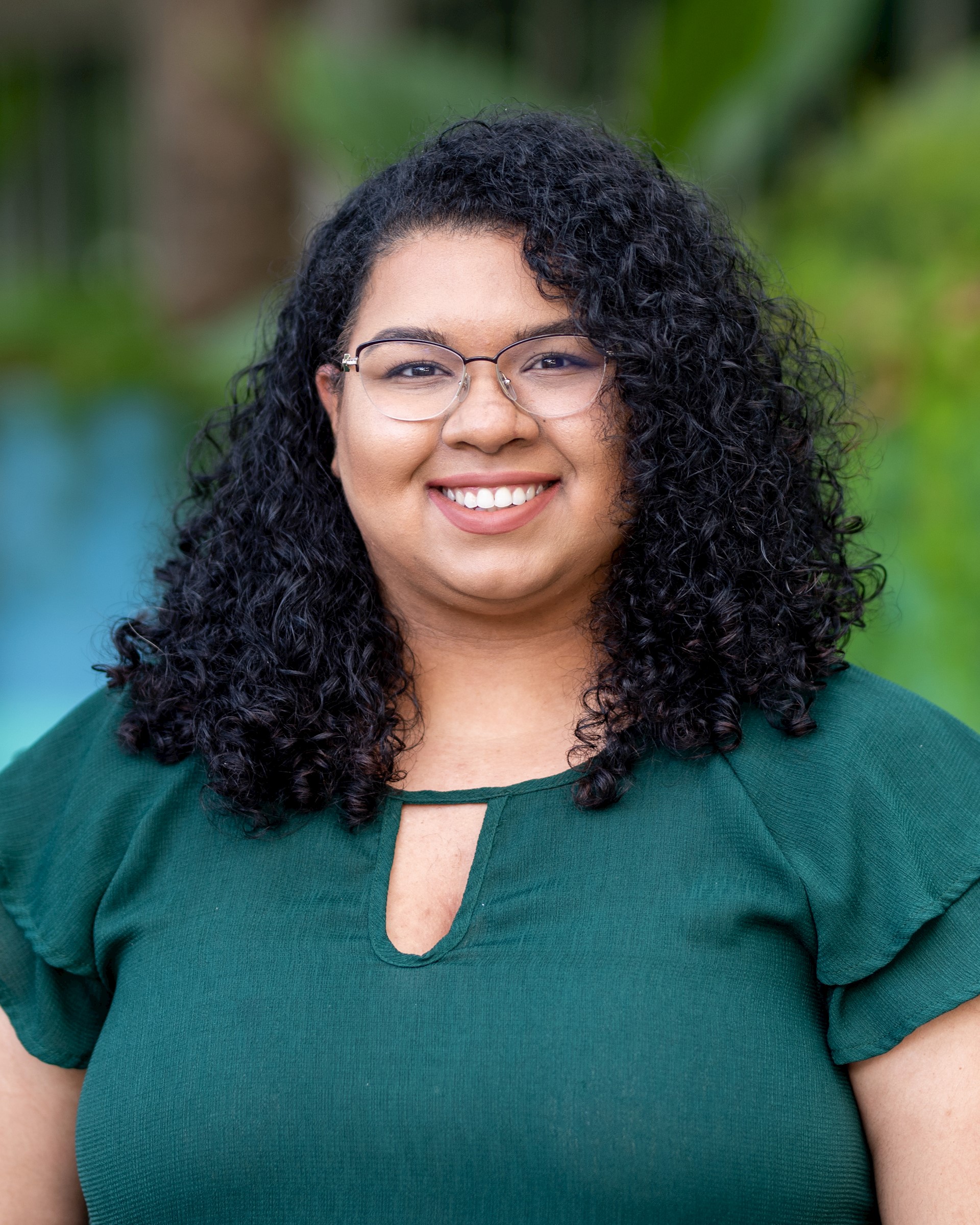 Fair skinned biracial woman with curly dark brown hair wearing glasses and a green shirt smiles at the camera