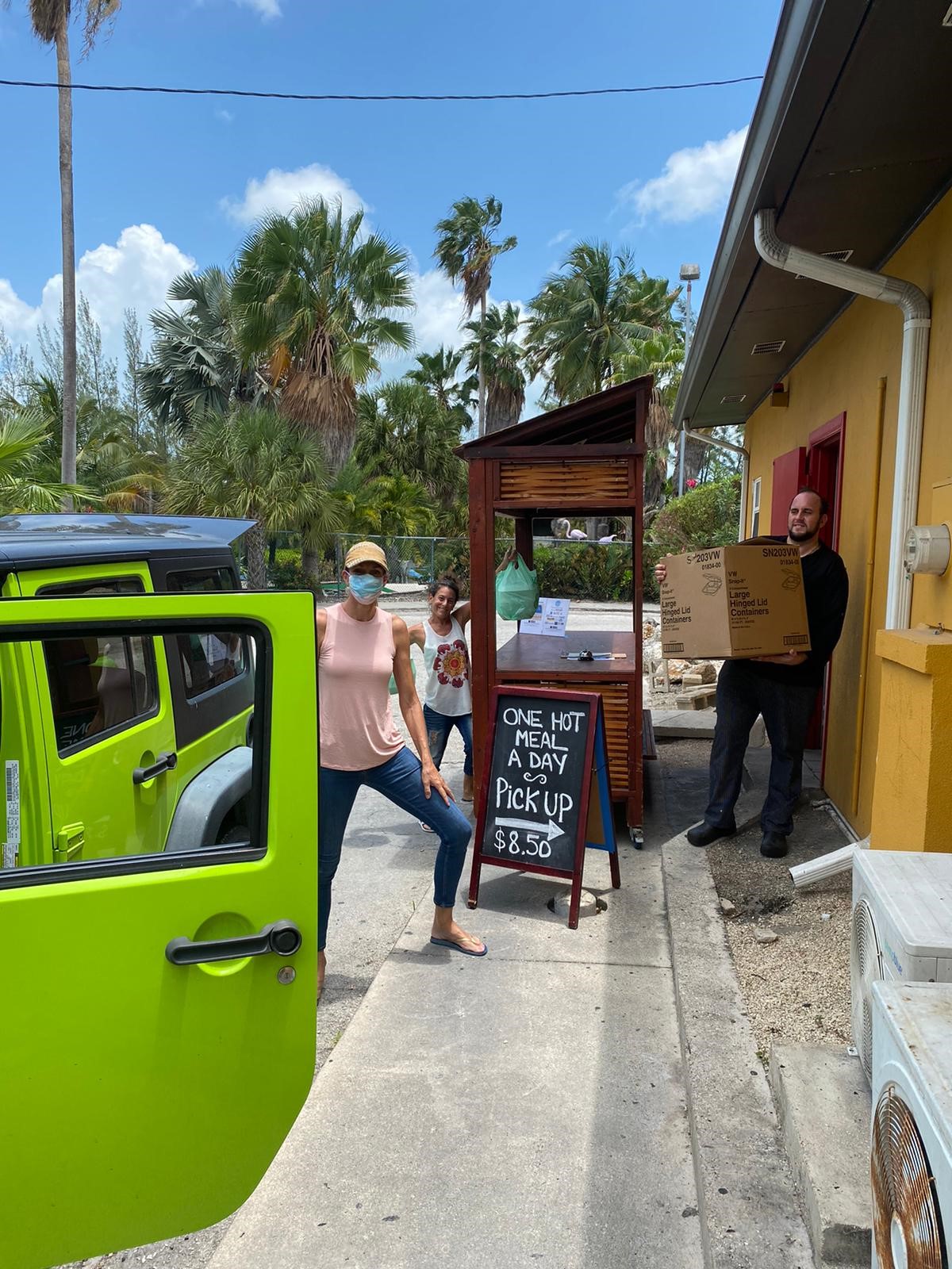 three-people-smiling-outside-a-kitchen-door-receiving-meals-to-deliver