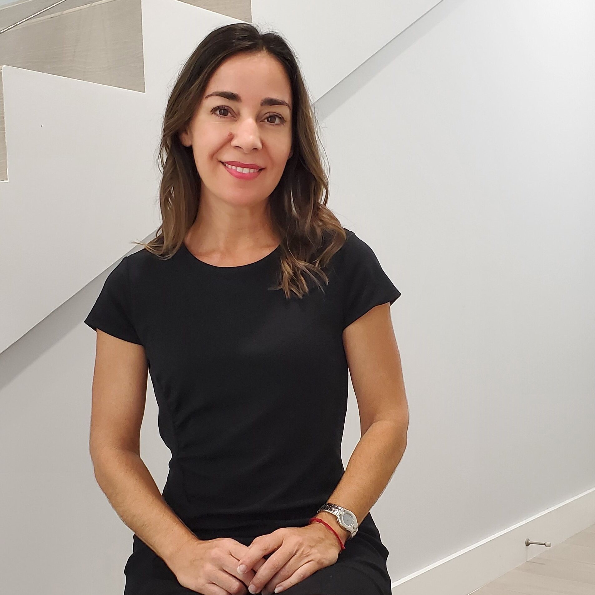 Light-skinned woman with brown hair wearing a black dress smiles at the camera 