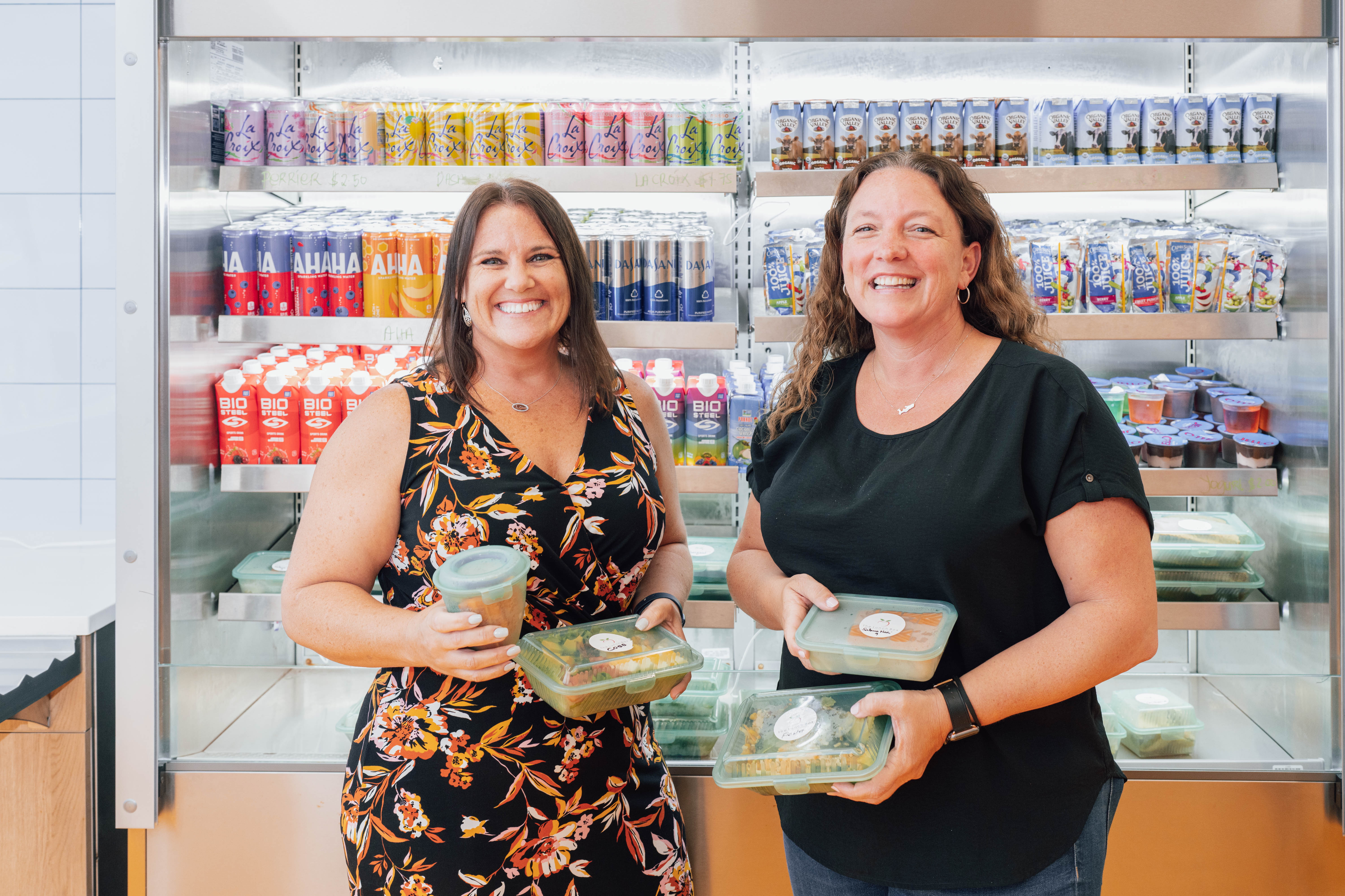 Two white woman stand in front of snack fridge
