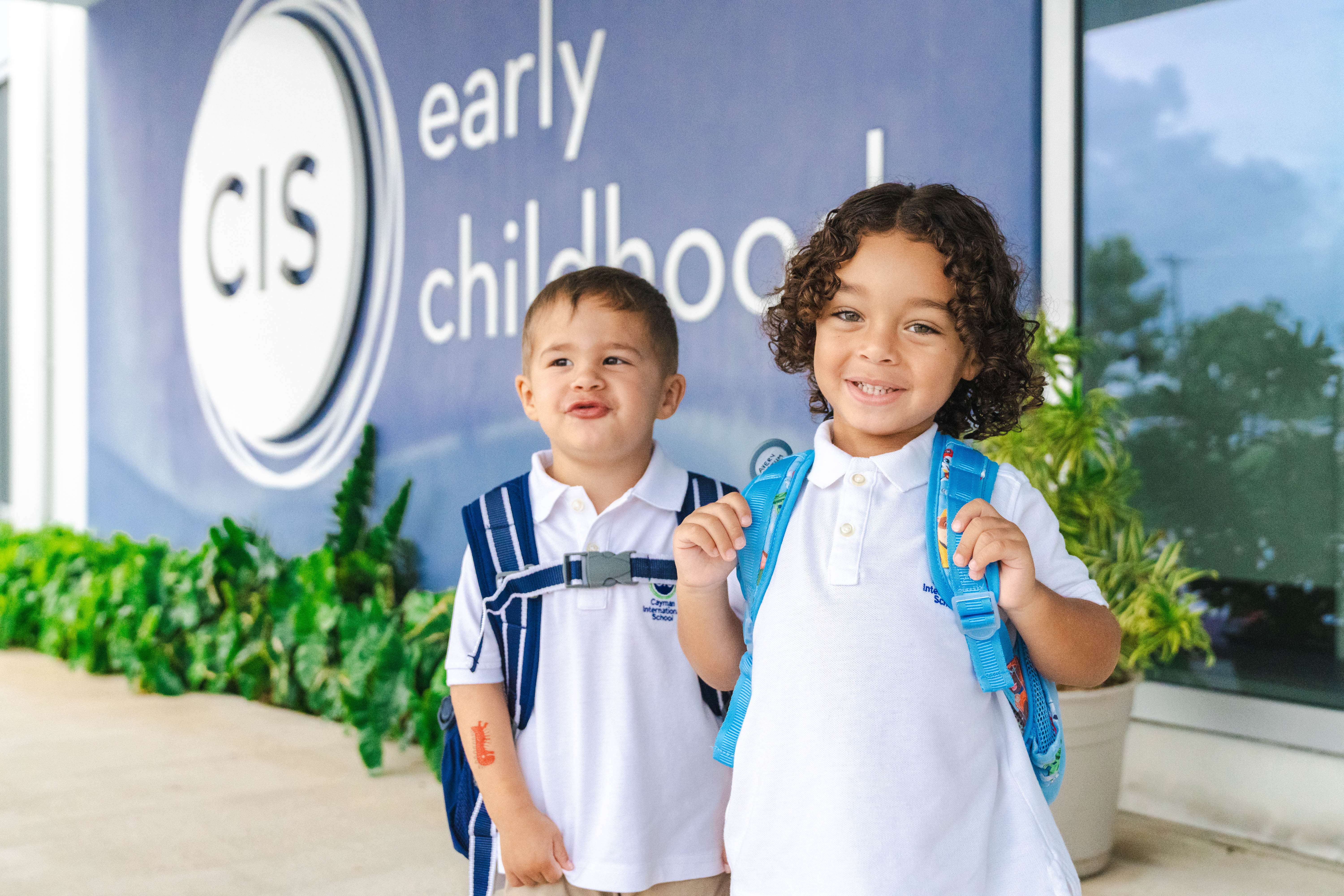 Two kids standing outside school with backpacks